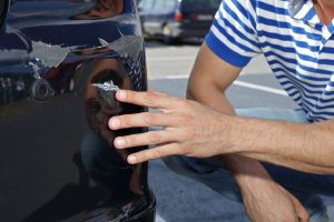 Person looking over damage to rear end of car; leaving the scene of an accident heightens potential consequences
