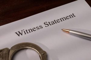 Making false witness statements is a criminal offense; witness statement with handcuffs and pen.